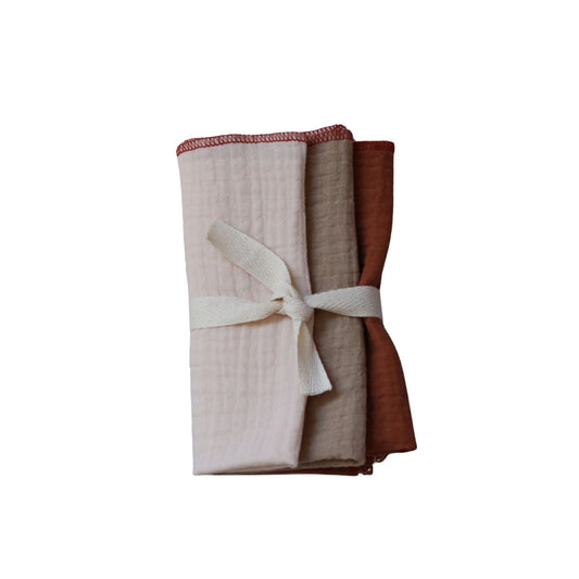 Zestaw trzech pieluszek dla noworodka uszytych z muślinu, związane wstążką na białym tle.