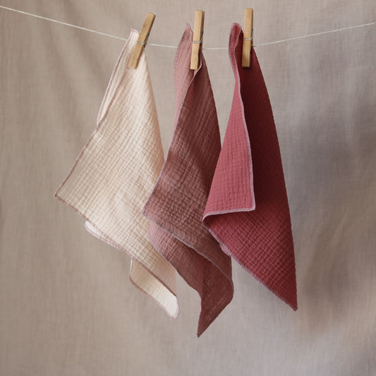 Trzy pieluszki muślinowe w kolorach kremowo różowych wiszące na sznurku 