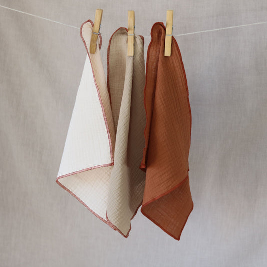 Trzy kolorowe zestawy pieluszek muślinowych do odbijania, suszące się na sznurku