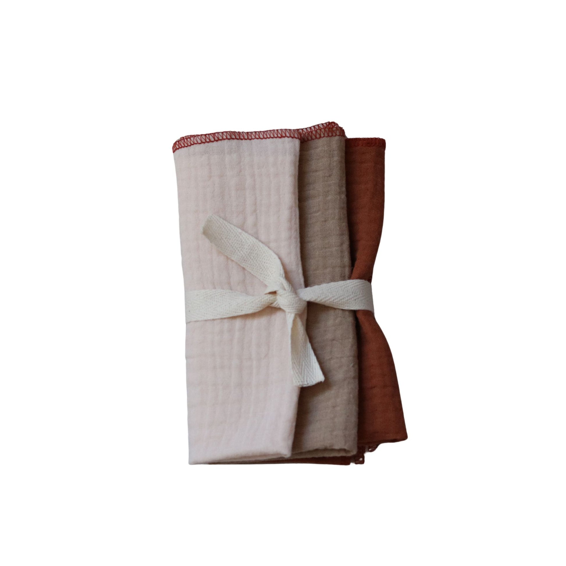 Zestaw trzech pieluszek dla noworodka uszytych z muślinu, związane wstążką na białym tle.